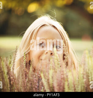 Nettes, kleines Mädchen versteckt sich hinter Heather Blumen Stockfoto