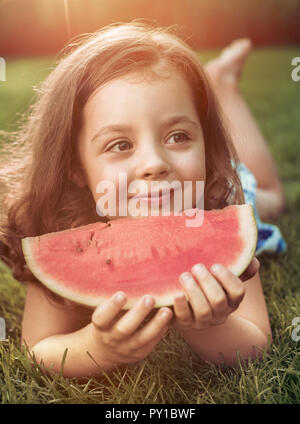 Closeup Portrait von lächelndes Kind holding Wassermelone Schicht im Garten Stockfoto