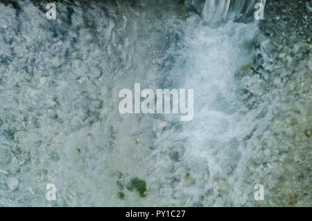 Nahaufnahme eines Ausbruchs von Wasser, kleiner Wasserfall auf der rechten Seite, kleine Wellen Wasser auf einem Fluss von frischem, kristallklarem Wasser. Stockfoto