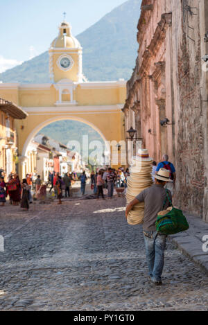 ANTIGUA, GUATEMALA - Februar 24, 2018: unbekannter Mann verkaufen Hüte Spaziergänge unter der berühmten Santa Catalina arch in der touristischen Stadt von Antigua, Guatemala Stockfoto