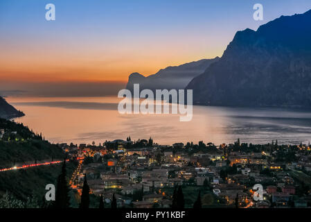 Night Skyline der Stadt im Tal mit Blick auf den See und die Berge, Riva del Garda, Italien Stockfoto