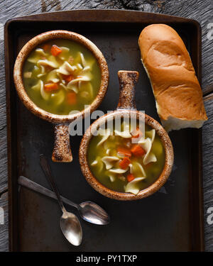 Zwei frische, hausgemachte Schüsseln mit Huhn Nudelsuppe mit einem Baguette und Löffel. Im Hochformat Nahaufnahme. Stockfoto