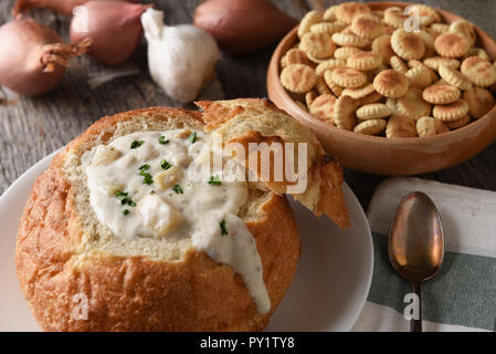 Nahaufnahme von einem Brot Schüssel von New England Clam Chowder. Eine Schüssel mit Oyster Cracker, Knoblauch und Zwiebeln im Hintergrund. Stockfoto