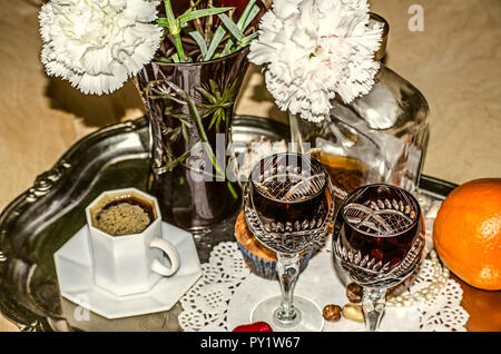 Crystal Vase mit Nelken, schwarzer Kaffee, alte Kristallgläser mit einer Flasche Likör, Muttern und eine Orange auf einem Tablett aus Neusilber Stockfoto