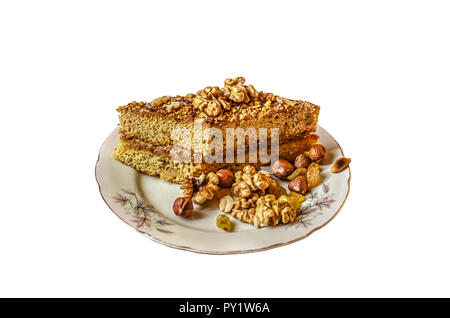 Stück Honigkuchen mit Muttern auf einem Porzellanteller mit Rosinen, Haselnüsse, Walnüsse und Erdnüsse auf weißem Hintergrund Stockfoto