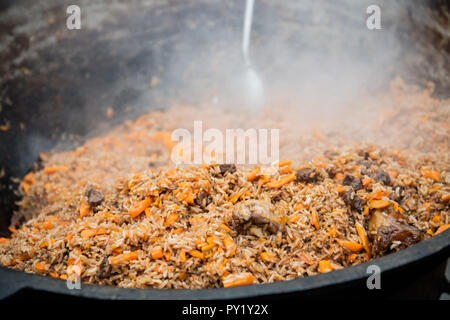 Lecker usbekischer Pilaw in einem Kessel auf Feuer im Freien bei Street Food Festival Stockfoto