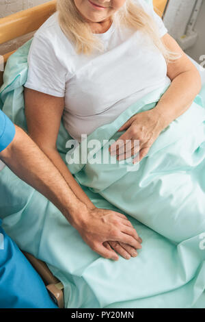 Teilweise mit Blick auf die männliche Krankenschwester die Hand der kranken älteren Frau im Krankenhaus Bett liegen Stockfoto