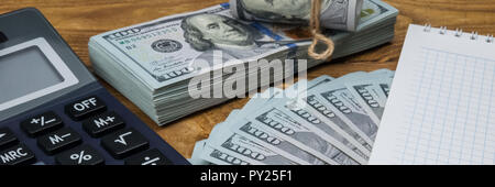 Ein Rechner, Dollar in einem Bundle, Rollen und Ventilator, ein Notizbuch und einen Stift auf einer hölzernen strukturierte Tabelle. Stockfoto