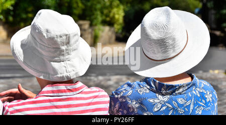 Zwei ältere reife Frauen sitzen im Gespräch an der Haltestelle an sehr heißen Hitzewelle Sommer Tag 2018 tragen weiße Hut in der Mittagssonne Haworth West Yorkshire England Großbritannien Stockfoto