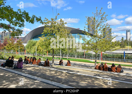 Schule Kinder reise Queen Elizabeth Olympic Park sitzen für die Mittagspause Blick auf Stratford London Aquatics Center Newham East London England Großbritannien Stockfoto