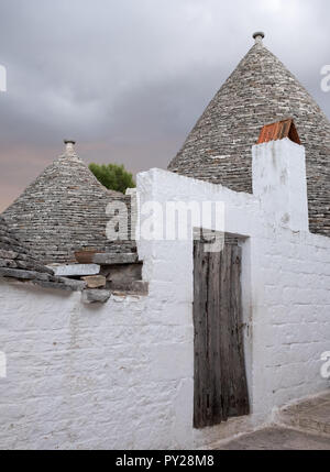 Alberobello, Italien. Weiß getünchten Konische überdachte Trulli Haus hinter weißen wahsed Wand, in die Stadt Alberobello in Apulien, Süditalien Stockfoto