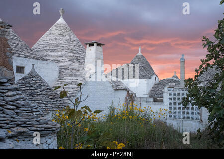 Traditionelle Trockenmauern konische überdachte Trulli auf der Straße in Aia Piccola Bereich von Alberobello, Apulien, Italien. Am frühen Morgen mit roten Himmel fotografiert. Stockfoto