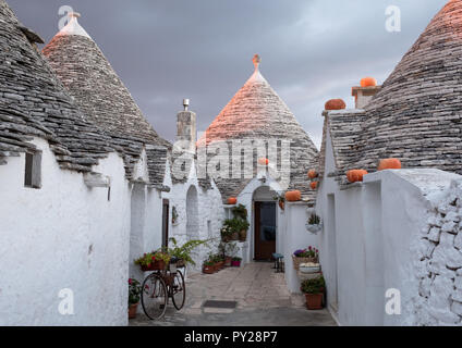 Trulli auf der Straße in Alberobello, Puglia, Italien. Kürbisse haben auf der Traufe platziert wurde Halloween zu feiern. Bei Sonnenaufgang fotografiert. Stockfoto