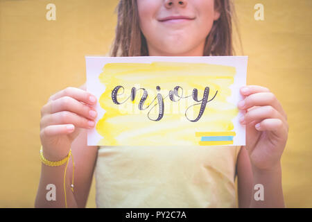 Junge hält ein Stück Papier mit dem Wort genießen Stockfoto