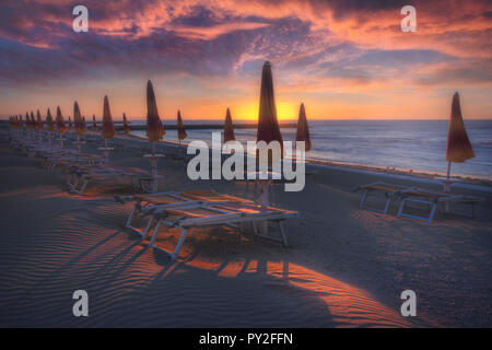 Liegestühle und Sonnenschirme am Strand bei Sonnenaufgang, Eraclea, Italien Stockfoto