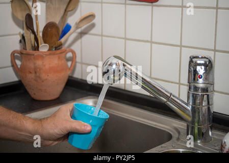 Des Menschen Hand Becher mit Wasser in einer Küche Stockfoto