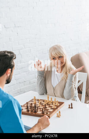 7/8 Schuß von jungen männlichen Betreuer schach spielen mit älteren Frau Stockfoto