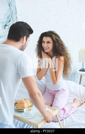 Junger Mann bringt das Frühstück zu glückliche junge Freundin im Bett Stockfoto