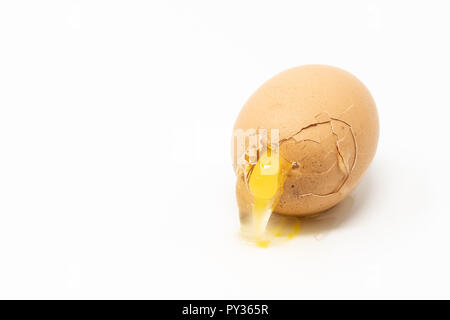 Kabelbruch im braunen Ei auf die weiße Fläche. Eigelb Auslaufen durch den Spalt. Stockfoto