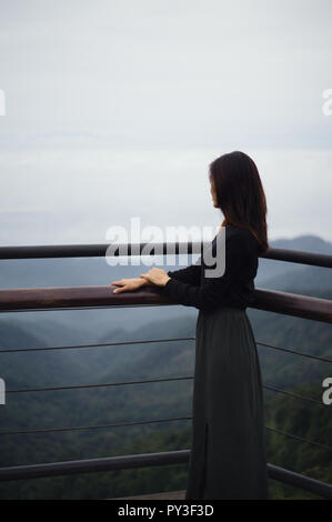 Jungen asiatischen (Vietnamesisch) Frau, die auf einen Balkon mit Blick auf die Berge in der Ferne in der Tam Dao, Northern Vietnam Stockfoto