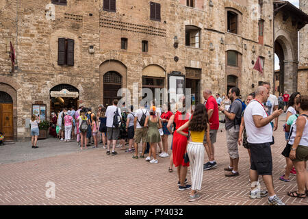 Eine sehr lange Warteschlange für Eis außerhalb der Gelateria Dondoli in Hilltop Stadt San Gimignano, Toskana, Italien Stockfoto