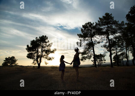 Gegenlicht einer Mutter und Tochter in einem Kiefernwald Mit gelbem Himmel Stockfoto