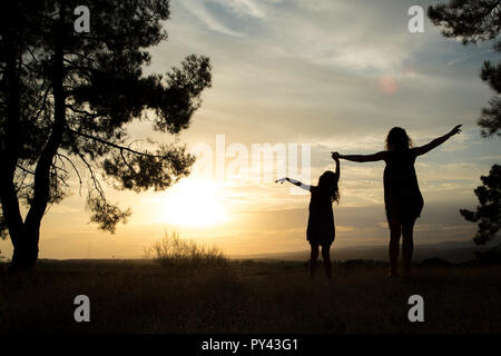 Gegenlicht einer Mutter und Tochter in einem Kiefernwald Mit gelbem Himmel Stockfoto