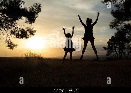 Gegenlicht einer Mutter und Tochter in einem Kiefernwald Mit gelbem Himmel Stockfoto