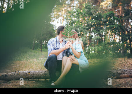 Paar küsst im Wald sitzt auf einem Ast und schließt mit einem Blatt Stockfoto