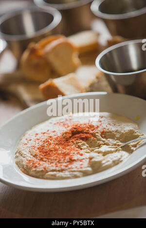 Eine Schüssel mit Stil Houmous (Hummus), die mit Paprika auf einem Tisch mit Brot im Sonnenlicht. Stockfoto