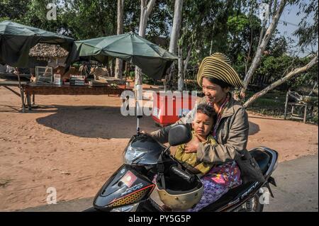 LAOS. Glückliche junge Mutter Motorrad fahren mit ihrem kleinen Sohn auf dem Schoß auf einer Landstraße in Laos. Stockfoto