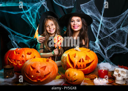 Halloween Konzept - schönen weißen Mutter und ihre Tochter in Hexe Kostüme Halloween Feiern mit Halloween Süßigkeiten und süße über Spider web Stockfoto