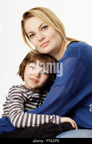 Eine lächelnde Junge und seine Mutter umarmt auf dem weißen Hintergrund. Konzept der Liebe und der Familie. Stockfoto