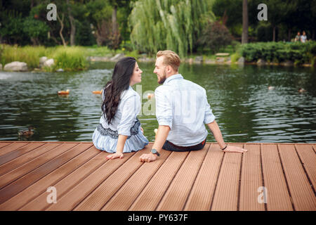 Schwangere Frau und ihr Mann in einem Park in der Nähe des Wasser umarmen Stockfoto