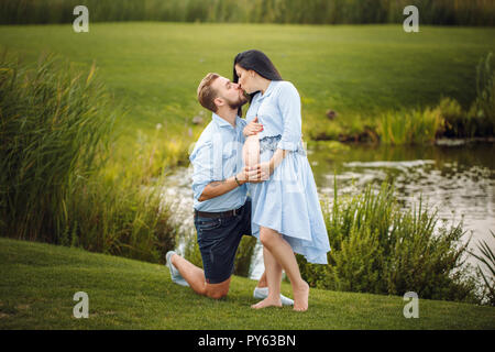 Schwangere Frau und ihr Mann in einem Park in der Nähe des Wasser umarmen Stockfoto