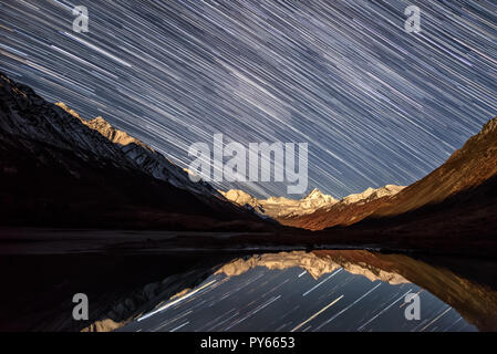 Tolle Nacht mit Sternen in Form von Tracks auf den Snowy Mountains, Berggipfel mit Hintergrundbeleuchtung aus dem Mondlicht und Reflexionen in der La Stockfoto