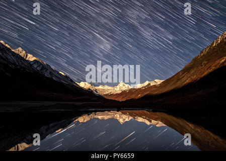 Tolle Nacht mit Sternen in Form von Tracks auf den Snowy Mountains, Berggipfel mit Hintergrundbeleuchtung aus dem Mondlicht und Reflexionen in der La Stockfoto