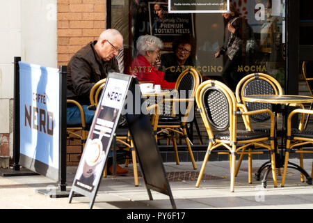 Ein Mann mittleren Alters saß außerhalb Cafe Nero Kaffee während zwei alte Frauen sitzen zusammen sind in der Entscheidung, welche in Dundee, UK zu bestellen. Stockfoto