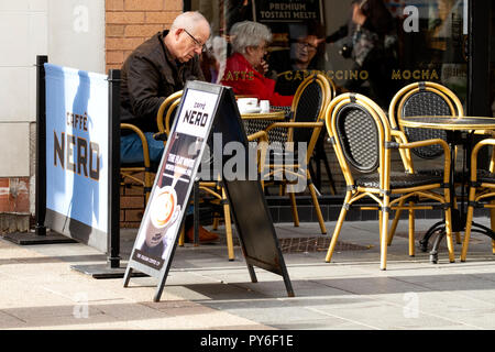 Ein Mann mittleren Alters saß außerhalb Cafe Nero Kaffee während zwei alte Frauen sitzen zusammen sind in der Entscheidung, welche in Dundee, UK zu bestellen. Stockfoto