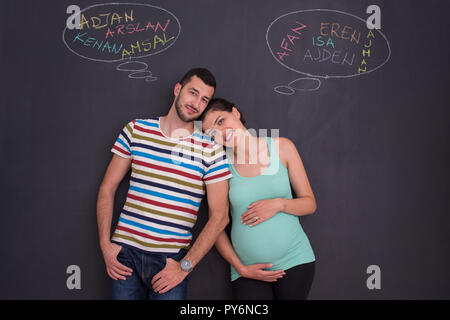 Junge schwangere paar Gedanken über Namen für Ihr ungeborenes Baby und sie schreiben auf eine Schwarze Schiefertafel Stockfoto