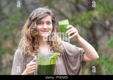 Junge Frau, Draußen, Draußen, holding Kunststoff Behälter für Blender Smoothie mit grünem Gemüse, bereit, mit Glas in der Hand zu trinken Stockfoto