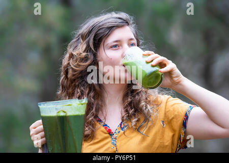 Nahaufnahme von einer jungen Frau, weiblich, außerhalb, Draußen, holding Kunststoff mixer Behälter, Trinken aus Glas grün Smoothie aus vegetab gemacht Stockfoto