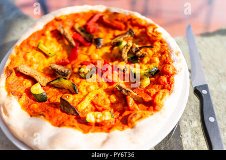 Nahaufnahme der frische Kruste handgefertigte Pizza auf Glas Tisch auf der Terrasse draußen in Italien mit roten Tomatensauce, Gemüse, Glas und Messer Stockfoto