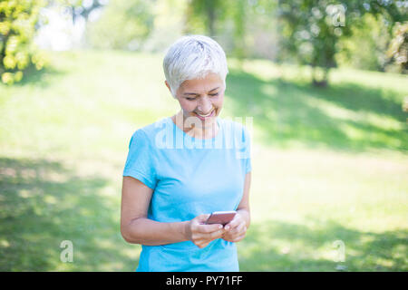Portrait der älteren Frau in Sportbekleidung mit smart phone Outdoor Stockfoto
