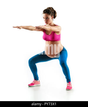 Sportliche schwangere Mädchen hocken, Sit-ups auf weißem Hintergrund. Konzept des gesunden Lebens Stockfoto