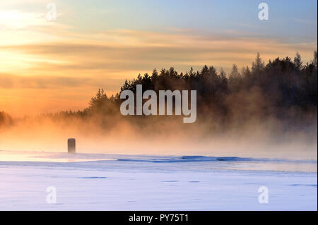 Nebel über dem Gefrierpunkt Fluss an einem kalten Winter. Aussicht auf den Sonnenuntergang. Stockfoto