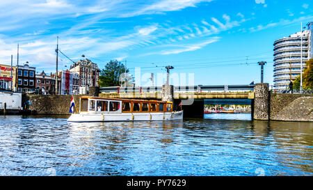 Altmodische Kanal Boot unter der Brücke am Stationsplein am Hauptbahnhof im Zentrum von Amsterdam und segeln in Richtung der Singelgracht Stockfoto