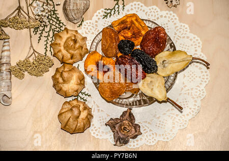 Kleine eclairs in der Nähe von Crystal Rosette mit getrockneten Früchten auf einem Papier figurine Serviette durch trockene Pflanzen und Muscheln auf Sperrholz umgeben Stockfoto