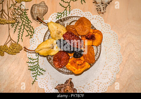 Crystal Rosette in der Nähe von kleinen eclairs mit getrockneten Früchten auf einem Papier figurine Serviette durch trockene Pflanzen und Muscheln auf Sperrholz umgeben Stockfoto