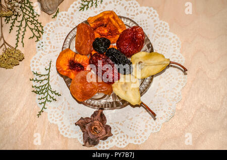 Dachte Serviette mit einem Crystal Rosette mit getrockneten Früchten gefüllt, und kleine eclairs durch trockene Pflanzen liegen auf Sperrholz umgeben Stockfoto